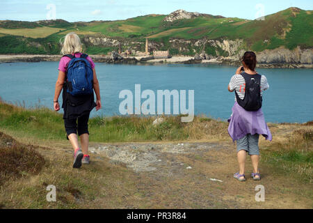 Two Women Hikers Walking & Taking Photos of the Old Abandoned Porth Wen Brickworks on Isle of Anglesey Coastal Path in Wales, UK. Stock Photo