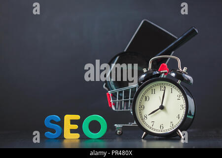 Colored letters of SEO with a magnifying glass, smartphone, gears in a basket on a black background Copyspace Stock Photo