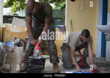 (Left) U.S. Marine Corps Sgt. David Tyson, 7th Engineer Support Battalion combat engineer, mixes grout as U.S. Air Force Staff Sgt. Zach Julian, 145th Airlift Wing water and fuel system maintenance craftsman, cuts tile during Pacific Angel (PAC ANGEL) 18-2 at Nguyen Hien Junior High School in in Phu Thinh town, Phu Ninh district, Vietnam, Sept. 11, 2018. During PAC ANGEL 18-2 civil engineers worked on repairs, refurbishing and upgrades to eight existing rural medical and school facilities. PAC ANGEL is a multilateral humanitarian assistance civil military engagement, which improves military-to Stock Photo