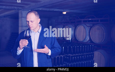 Confident male winemaker holding glass of red wine, checking it in wine cellar Stock Photo