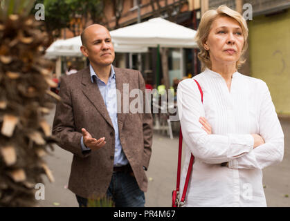 closeup of angry retiree blond woman being sad with man outdoors Stock Photo