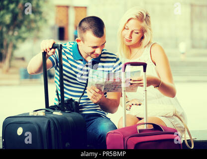 Positive young traveling couple searching for direction using paper map in town Stock Photo