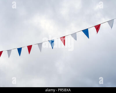Red, white and blue festive bunting flags against sky background. Triangle shapes against cloudy sky. Stock Photo