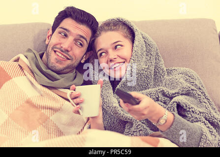 Loving young couple snuggling on sofa with cup of tea watching TV Stock Photo