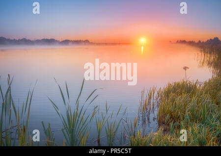 Autumn sunrise over the lake which is covered with fog early in the morning Stock Photo