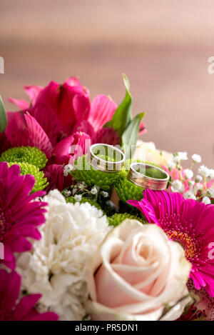 Two wedding rings on flowers of a bridal colorful bouquet with purple daisies, white carnations and pale pink roses. Stock Photo