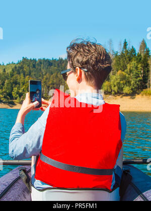 Young woman taking selfie with smart phone while kayaking on the Lokvarsko lake in Gorski kotar, Croatia. Girl enjoying adventurous experience on Stock Photo