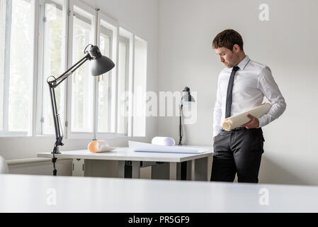 Experienced businessman analyzing important blueprints standing at white desk in the office. Stock Photo