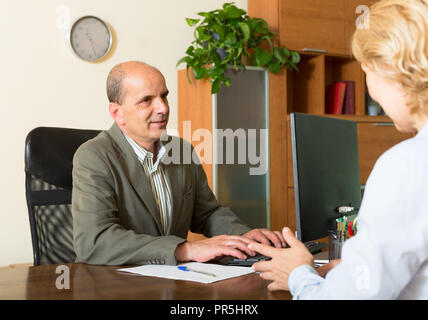 Elderly female client talking with manager at the table in notary's office Stock Photo