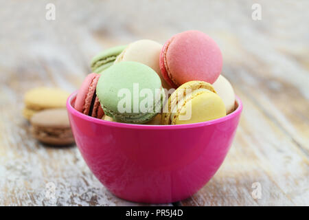 Colorful crunchy macaroons in pink bowl on rustic wooden surface with copy space Stock Photo