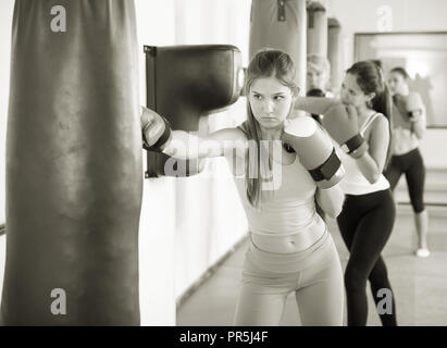 portrait of young female is doing exercises with punching bag in sporty gym. Stock Photo