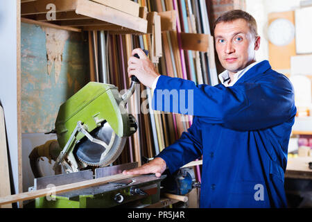 Smiling man wearing protective workwear operating circular saw in wood workshop Stock Photo