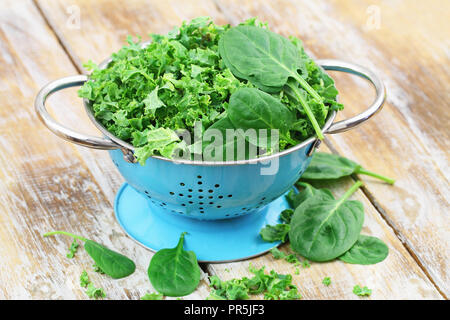 Shredded raw kale and spinach baby leaves in blue colander on rustic wooden surface with copy space Stock Photo