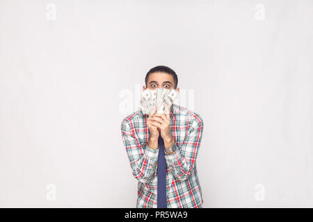 Portrait of rich handsome young adult businessman in colorful checkered shirt with blue tie standing and showing fan of dollars with big crazy eyes. I