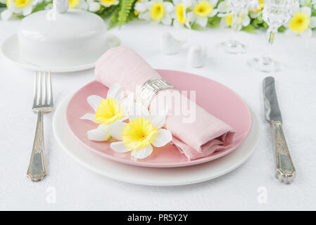 Classic serving for a Easter dinner with white and pink porcelain plates, silverware and spring flowers on a white tablecloth Stock Photo