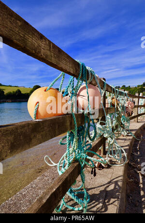 Fishing floats tied to the fence near the entrance to Pascoes Boat Yard, Roseland, Cornwall Stock Photo