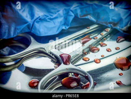 Gloves blue and scissors stained with blood on a tray in an operating theater, conceptual image Stock Photo
