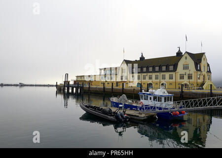 Historic Harbour Building In The Norwegian Municipal Architectural Style On The Waterfront In Harstad, A Thick Bank Of Sea Fog Behind, Norway. Stock Photo