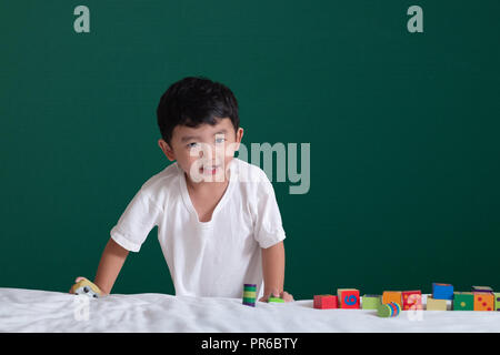 3 years old Asian boy play toy or square block puzzle on green chalkboard or school board background, kid lying learn by playing block shape or pieces Stock Photo