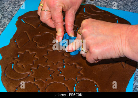Female hand making the traditional Christmas cookies. Raw dough is being punched out for the holiday cookies on a blue underlay. Preparing gingerbread Stock Photo