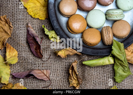 top view - rustic plate of macaroons on woven natural material, surrounded by autumn leaves Stock Photo