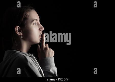 scared girl show silence gesture on black background with copy space Stock Photo