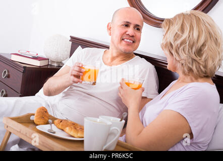 Positive smiling mature spouses having healthy breakfast in bed in the morning Stock Photo