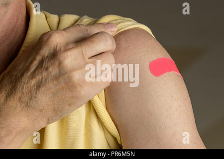 Senior man holding up shirt after flu injection Stock Photo