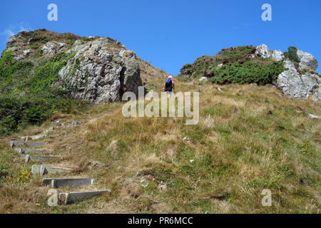Woman Hiker Walking up Steps West Along the Coast from Porth Llanlleiana Bay on Isle of Anglesey Coastal Path in Wales, UK. Stock Photo