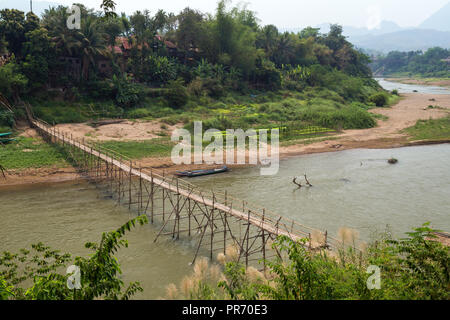 View of a bamboo bridge over Nam Khan River at low tide and lush riverbank in Luang Prabang, Laos, on a sunny day. Stock Photo
