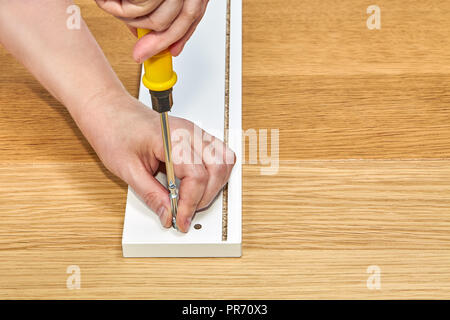 Flat pack furniture assembly, assembler tightens dowel pin bolt, using hand tool, closeap. Stock Photo