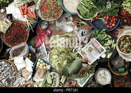 Woman reading newspaper among her fruit and vegetable stall at Siti Khadijah Market in Kota Bharu, Malaysia. Stock Photo