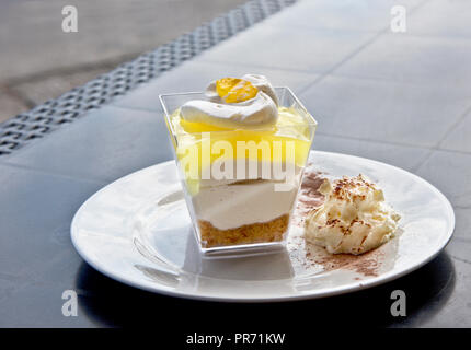 Lemon dessert, lemon trifle, cheesecake, whipped cream, parfait. Tasty delicious cake served in glass on a grey background. Stock Photo