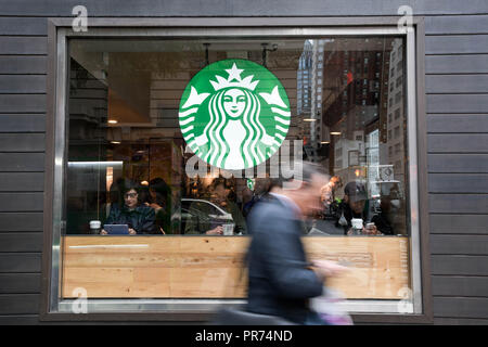 A businessman checks his mobile phone while walking past a Starbucks on Fifth Avenue in New York City on a cloudy September morning. Stock Photo