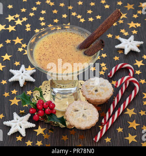 Christmas eggnog traditional drink with mince pies, candy canes, star decorations and winter holly on rustic oak table background. Festive theme. Stock Photo