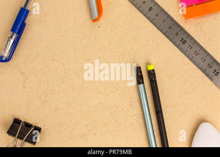 Stationery (pens, pencils, ruler, eraser, clamp and stickers) lie on the sand. Top view