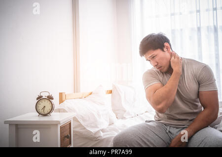 Male woke up by alarm clock having neck pain from sleeping Stock Photo