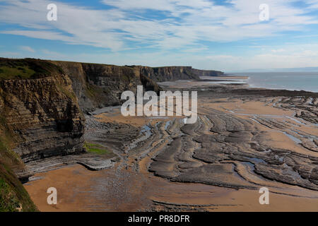 View south along the cliffs towards Monk nash point with the tide fully out exposing the eroded roack layers amid the sands on this 'Heritage' coast. Stock Photo