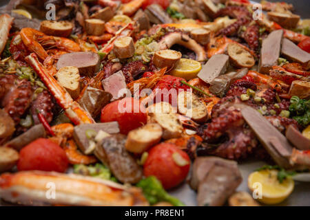Gourmet seafood Valencia paella with fresh octopus, langoustine, clams, mussels and squid on savory saffron rice with peas and lemon slices, close up  Stock Photo