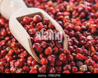 Wooden scoop filled with dried pink pepper berries. Close up view of pink peppercorn. Stock Photo