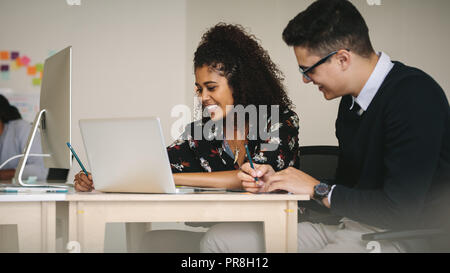 Businessman and woman discussing work and writing notes sitting in office. Business partners working together sitting at the desk with laptop computer Stock Photo