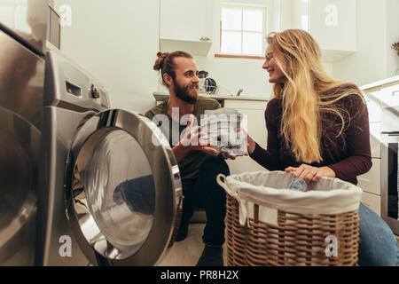 Happy couple putting clothes in washing machine. Couple using a front loading washing machine to wash laundry. Stock Photo