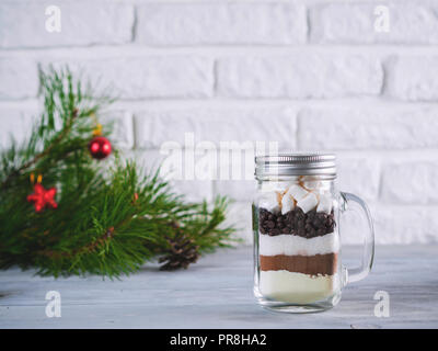 Hot chocolate mix in mason jar on gray table and white brick wall.Homemade mix from cocoa,dry milk,sugar,chocolate chips,marshmallows.Christmas andwinter holiday budget-friendly gifts idea.Copy space Stock Photo