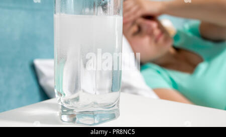 Closeup image of aspirin in water against woman suffering from headache Stock Photo