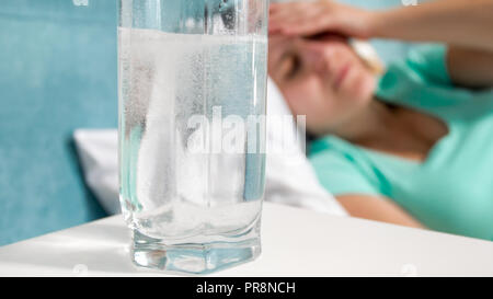 Closeup image of glass of carbonated water on bedside table next to sick woman lying in bed Stock Photo