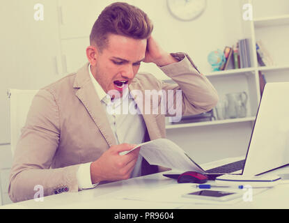 Upset young man having business problems with documents at workplace Stock Photo