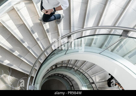 Looking down on an spiral staircase as a man eating a sandwich walks down Stock Photo