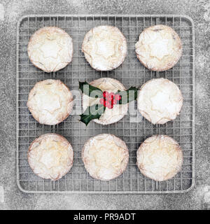Traditional Christmas mince pies on a baking rack with holly and berry leaf sprig with icing sugar dusting. Flat lay. Stock Photo