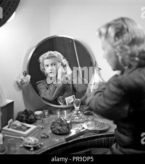 Woman combing her hair. Actress Irma Christenson, 1915-1993. Pictured here while sitting in at a makeup table looking at herself in the mirror while putting on her earrings. Sweden 1945.  Photo Kristoffersson R45-3 Stock Photo