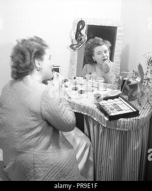 Cosmetics in the 1940s. A young woman at home is sitting at a make up desk and looking at herself in the mirror while putting on lipstick. There are many different kinds of cosmectics lying on the table in front of her. Sweden 1947.  Photo Kristoffersson AB3-8 Stock Photo